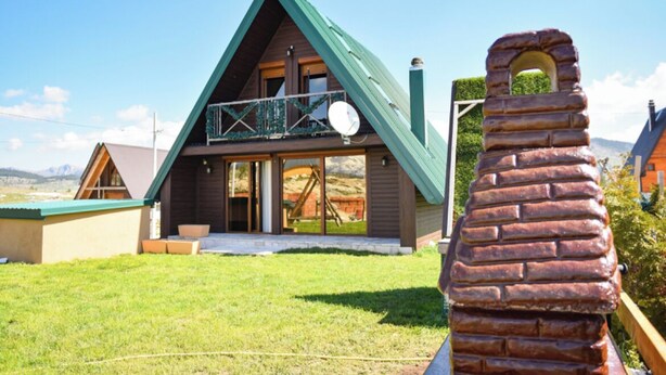 Una cabaña de dos pisos con techo verde, un balcón y una chimenea.