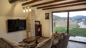 Un salón acogedor con chimenea de piedra, un ventanal que ofrece vistas a un paisaje rural y un mueble moderno para el entretenimiento.