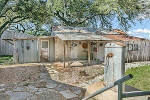 Un bâtiment rustique avec un toit en tôle ondulée, une porte en bois portant l’inscription « Buanderie » et un petit espace extérieur aménagé pour s’asseoir.