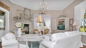 Una sala de estar acogedora con chimenea, muebles blancos y una araña.