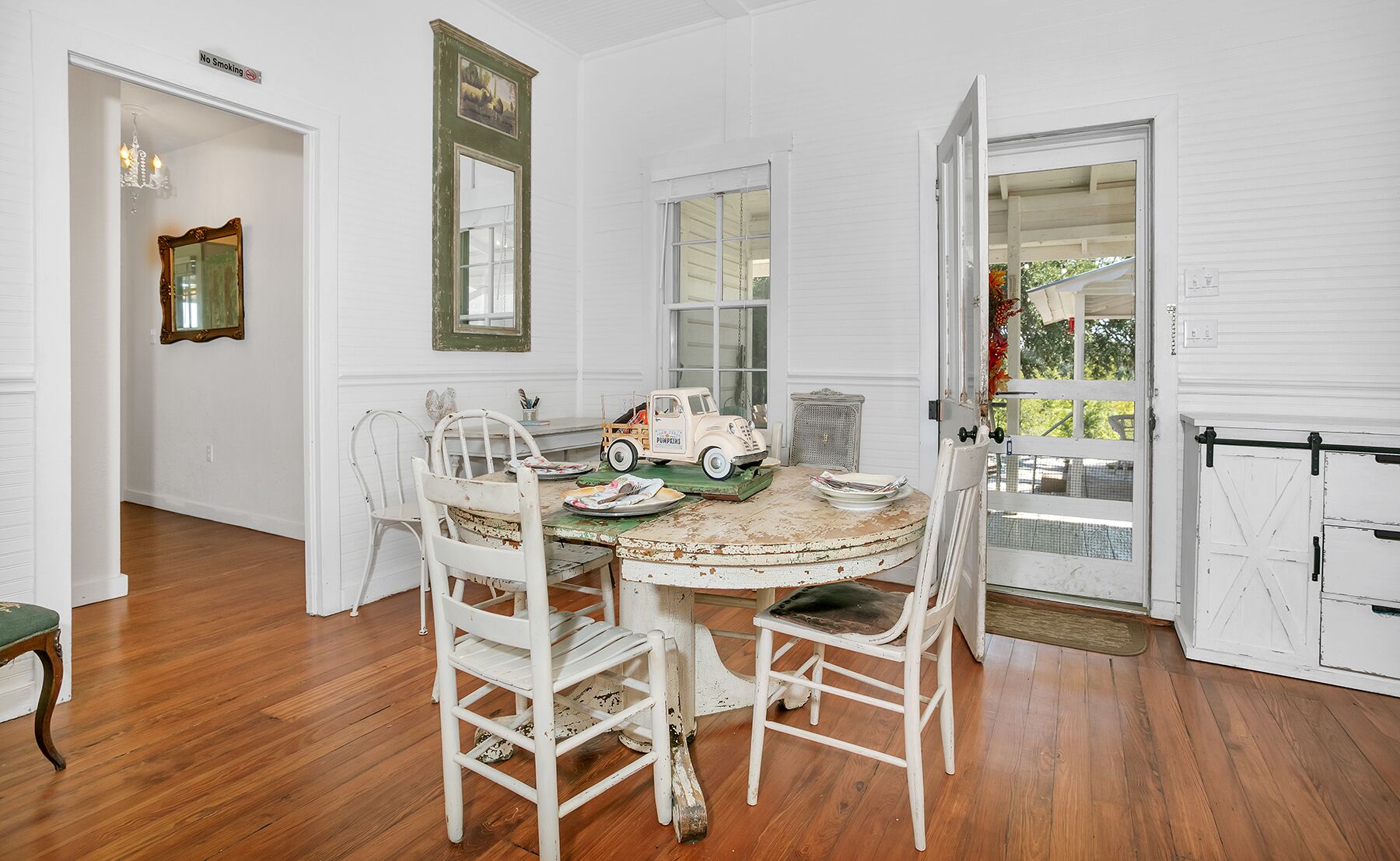 A dining area with a round table, white chairs, and a vintage toy truck centerpiece.