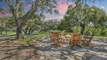 An outdoor seating area with stone flooring, wooden chairs, and a fire pit.