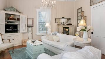 A room with a white sofa, a small table with a lamp, a vintage television, and a chandelier.