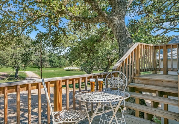 Une terrasse en bois avec une table et des chaises en métal, donnant sur une pelouse et des arbres.