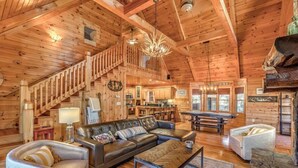 Un intérieur spacieux de chalet en bois, comprenant un salon, un coin repas, une cuisine et un escalier menant à un niveau supérieur.