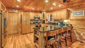L’intérieur d’une cabane en bois comprend une cuisine avec des meubles en bois, un îlot central doté de tabourets de bar et une horloge murale.