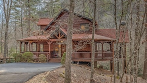 A rustic cabin with a porch, surrounded by trees.