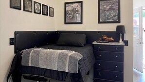 A bedroom with a black headboard, a bed with a gray and white blanket, a dresser with drawers, and four framed pictures on the wall. - Biker's Bungalow - Near Mendenhall Glacier and Auke Bay Offering DISCOUNT ON TOURS! (Juneau)