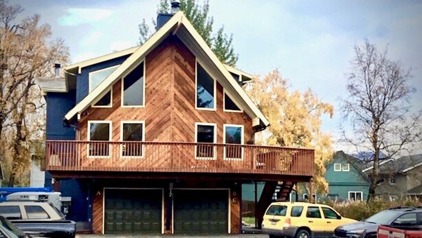 A two-story house with a wooden exterior, a balcony on the upper floor, and a garage with two doors. - Sand Lake Jewel - Near Airport, Shopping and the Best Sushi in Town! (Anchorage)