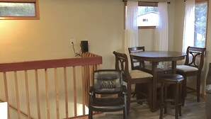 Un coin repas avec une table et des chaises en bois, une rambarde en bois et une fenêtre avec des rideaux.