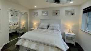 A neatly arranged bedroom with a large bed, two bedside tables with lamps, a ceiling light, and a full-length mirror.