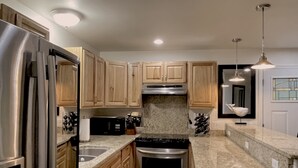 A modern kitchen with stainless steel appliances, wooden cabinets, granite countertops, and pendant lighting.