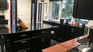 A modern kitchen with black cabinetry, a granite countertop, and a window with a view of trees.