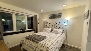 Ein Schlafzimmer mit einem Bett, einem Fenster, einer Stehlampe und einem Bild an der Wand.