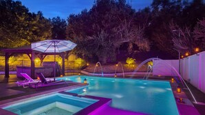 Una piscina con jacuzzi, sillas de descanso y una zona cubierta con toldo.