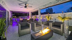 Un patio al aire libre con mobiliario de mimbre, una chimenea y una iluminación ambiental.