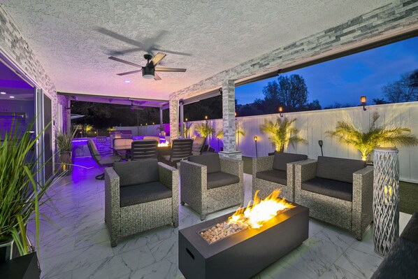 An outdoor patio with wicker furniture, a fire feature, and ambient lighting.