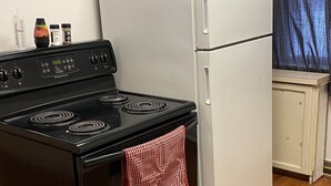 A kitchen with a black stove, a white refrigerator, wooden flooring, and a window with blue curtains.