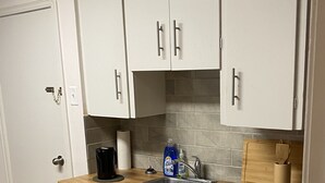 A compact kitchen with white cabinets, a wooden countertop, a sink, and a coffee maker.