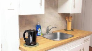 A kitchen with a wooden countertop, a black coffee maker, a stainless steel sink, and a set of wooden utensils in a holder.