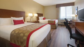 Ein Hotelzimmer mit zwei Betten, einem Schreibtisch, einem Stuhl und einem Fernseher.