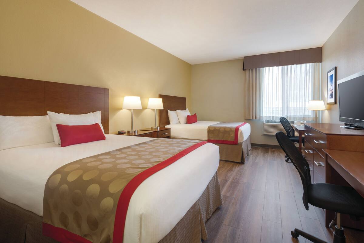 Habitación de hotel con dos camas, un escritorio, una silla y un televisor.
