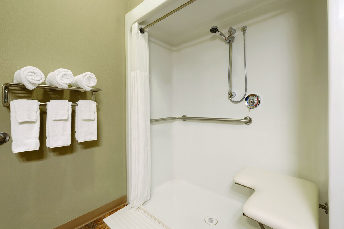 A shower with a handheld showerhead and a grab bar, a white toilet, and a towel rack with three towels.