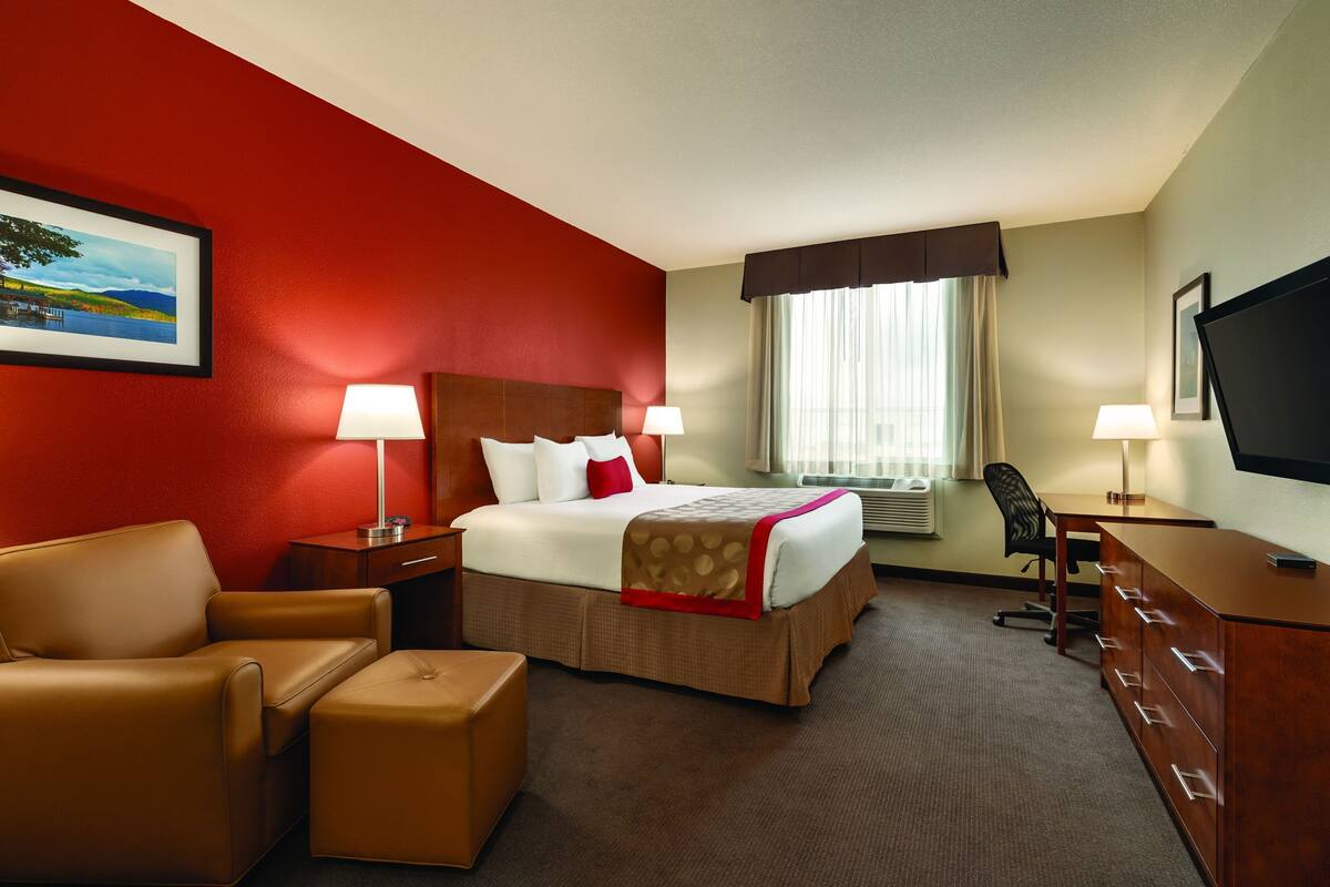 Una habitación de hotel con cama, escritorio, silla, televisor y ventana con cortinas.