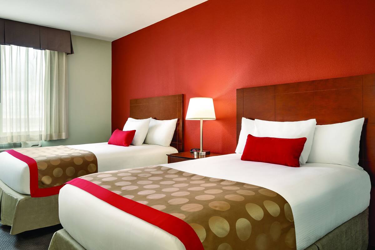 Una habitación de hotel con dos camas, una pared de acento roja y una ventana con cortinas.