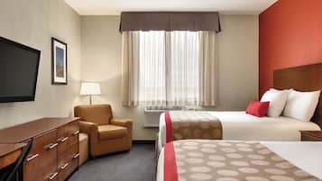Habitación de hotel con cama, silla, escritorio, televisor y ventana con cortinas.