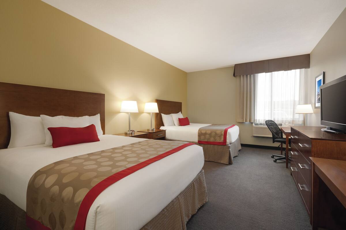Habitación de hotel con dos camas, un escritorio, una silla, un televisor y un equipo de aire acondicionado.