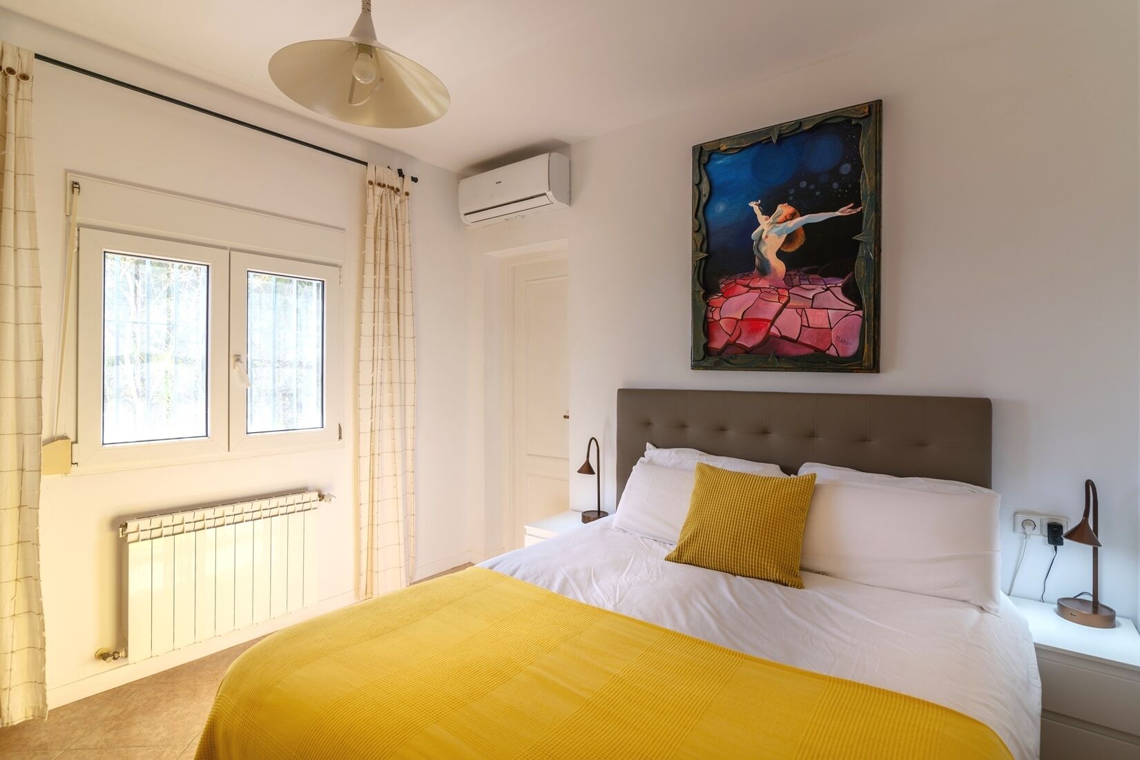 Un dormitorio con cama, ventana, equipo de aire acondicionado y un cuadro en la pared.