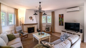 A living room with a fireplace, sofa, TV, and artwork. - House of the Rising Sun - Luxury villa with private pool and stunning sea views (Sayalonga)