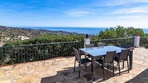 A patio with a table and chairs, overlooking a scenic landscape with hills and the sea. - House of the Rising Sun - Luxury villa with private pool and stunning sea views (Sayalonga)