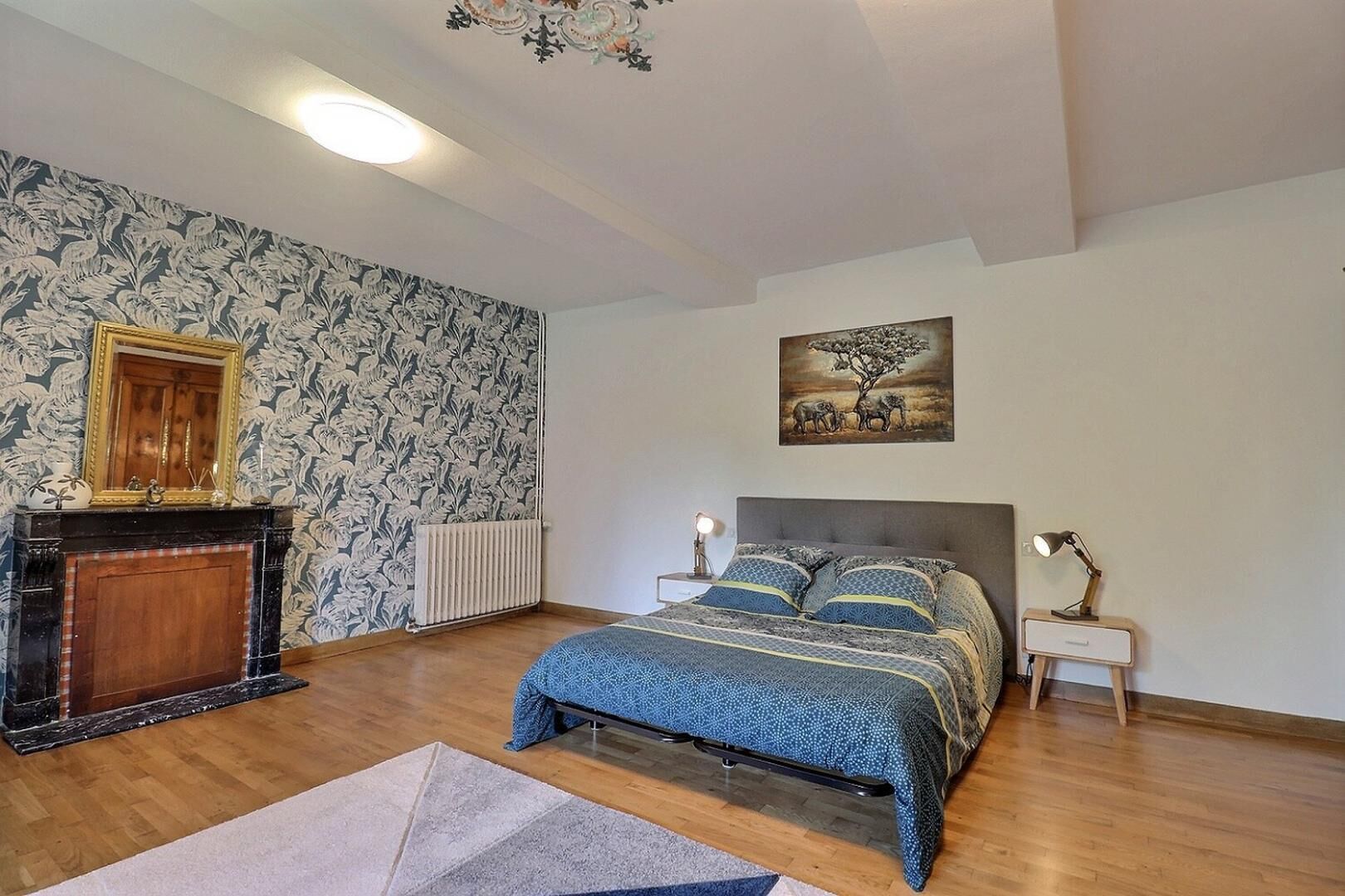 Een slaapkamer met een bed, een open haard, een radiator, een schilderij en een nachtkastje met een lamp.
