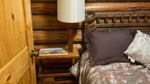 Ein Holzhütten-Zimmer mit einem Etagenbett, einem Nachttisch mit Lampe und einem Buch.