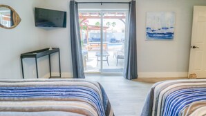 A hotel room with two beds, a TV, a desk, and a view of the outdoor patio. - Stay 7+ Nights for 10% Off: Isla Breeze, Your Easeful Escape (South Padre Island)