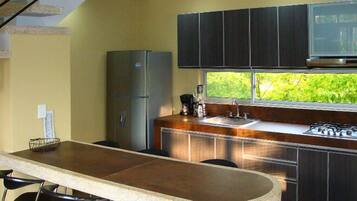 Una cocina compacta con estufa a gas integrada, un refrigerador y ventana con vista a la vegetación.