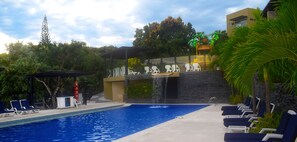 Ein Swimmingpool mit Liegestühlen, einem Wasserfall und einer überdachten Sitzgelegenheit.