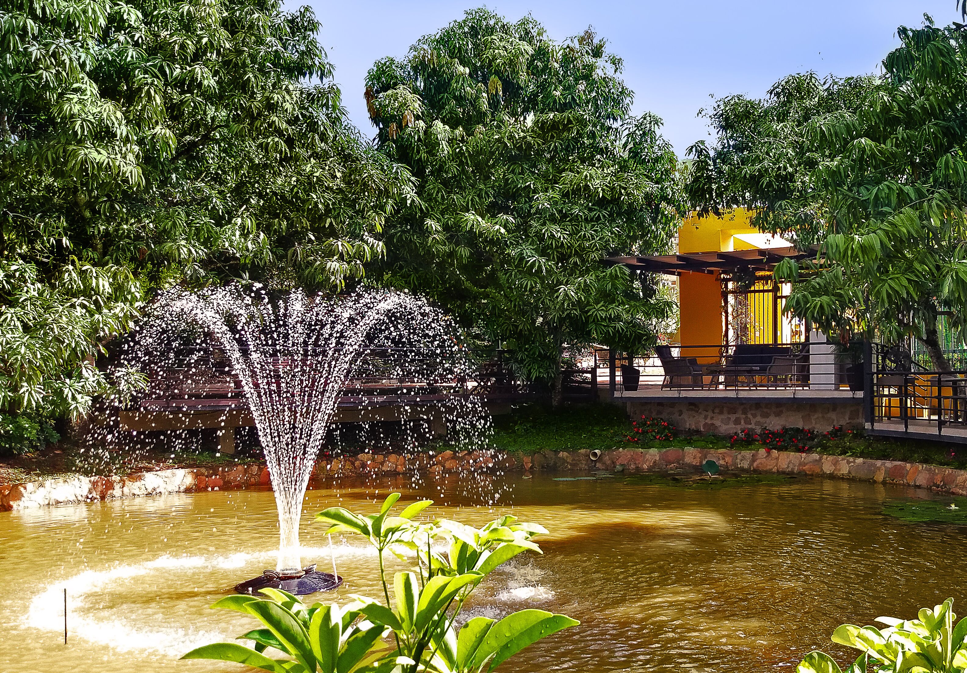 A fountain in a park with a yellow structure in the background.