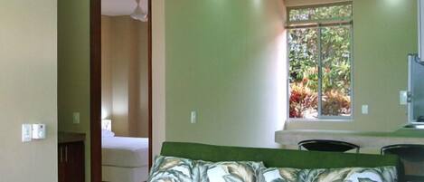 A room with a green sofa, a window with a view of greenery, and a ceiling with green lighting.
