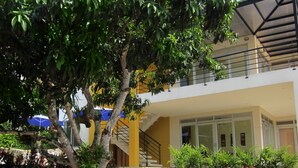 Un edificio de varios niveles con una escalera que conduce a un balcón, rodeado de abundante follaje y plantas en flor.