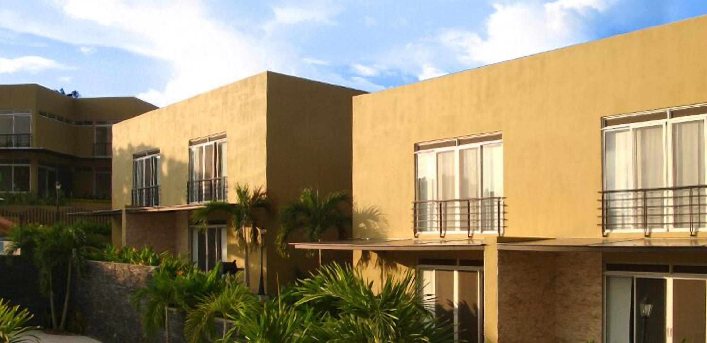 Un edificio de varios pisos con balcones y ventanas amplias, rodeado de vegetación.