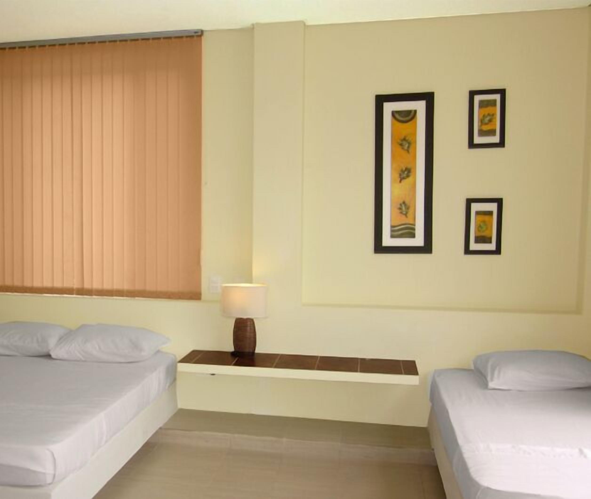 A hotel room with two beds, a nightstand with a lamp, and two framed pictures on the wall.