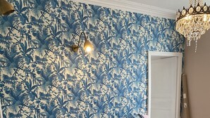 Un salón acogedor con un sofá rosa, cojines estampados y un papel tapiz floral azul.