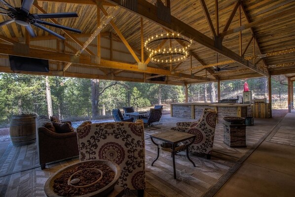 A covered outdoor seating area with rustic wooden beams, a chandelier, and a view of the surrounding forest. - Stunning home on 7 acres with 5400sf of indoor/outdoor living space (Hermosa)