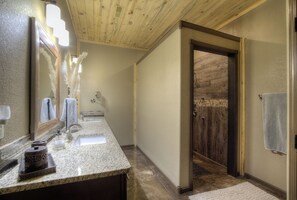 A bathroom with a granite countertop, a mirror, a towel rack, and a wooden door leading to a shower area. - Stunning home on 7 acres with 5400sf of indoor/outdoor living space (Hermosa)
