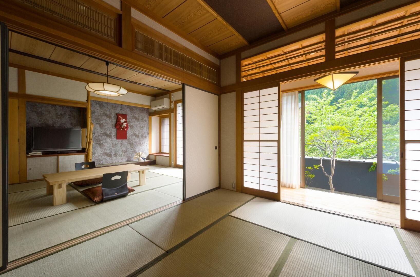 A traditional Japanese room with tatami flooring, a low table, a television, and a sliding door to a garden.