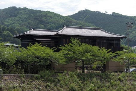 A traditional Japanese building with a tiled roof, surrounded by greenery and hills.