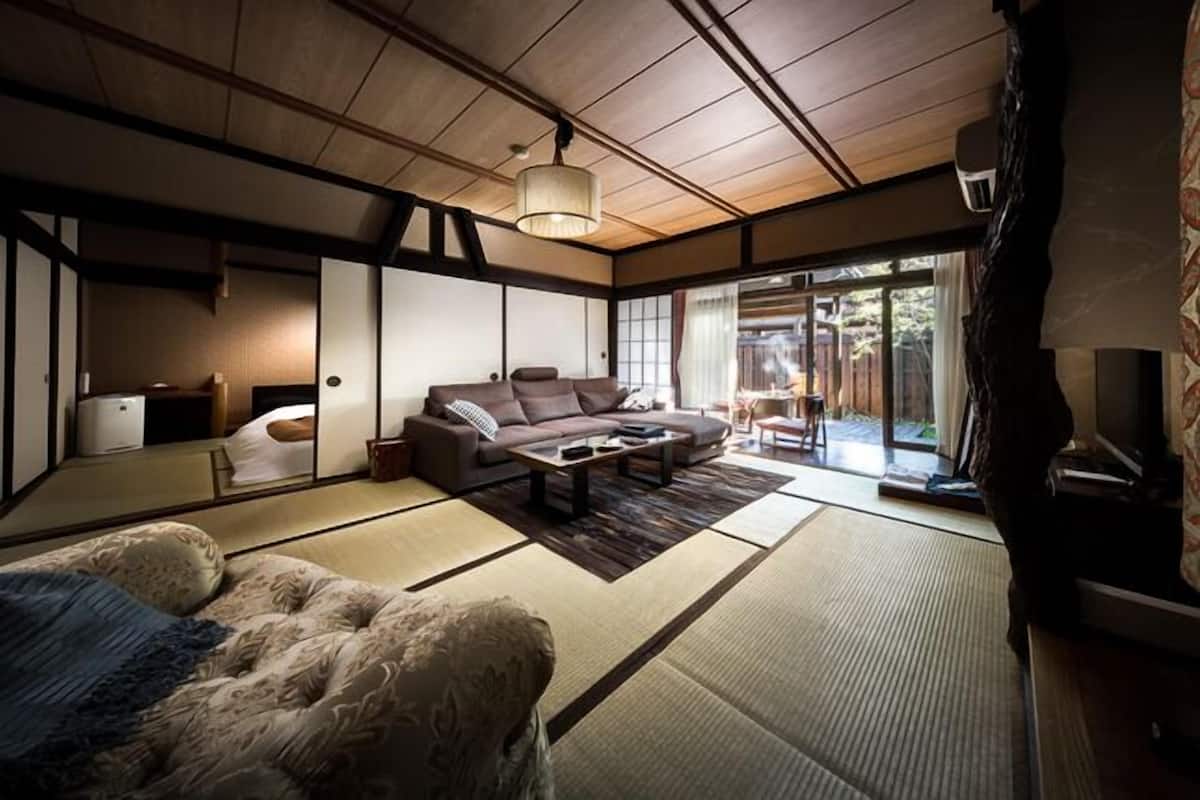 A traditional Japanese-style room with tatami flooring, a sofa, a coffee table, and sliding doors leading to an outdoor area.